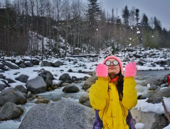 Woman wearing warm clothing sitting on rock during snowfall