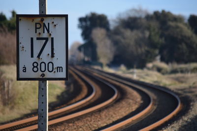 Close-up of road sign by railroad tracks against sky