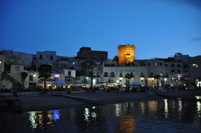 Illuminated buildings against blue sky at night