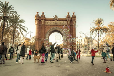 People playing with soap bubbles at arc de triomf against sky