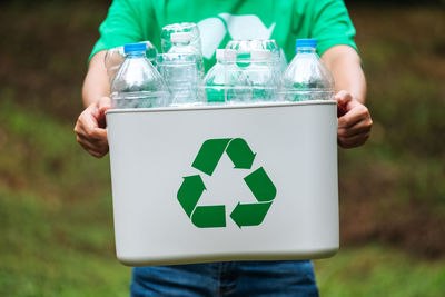 A woman holding a recycle bin with plastic bottles in the outdoors