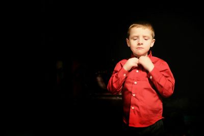 Cute boy in red shirt standing in darkroom