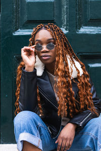 Confident african american female in trendy outfit and sunglasses with long braided hair looking away in city street