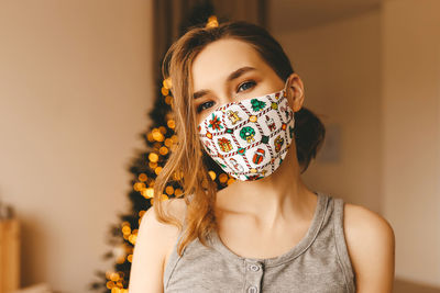 Close-up portrait of a girl in a christmas protective mask near the christmas tree at home