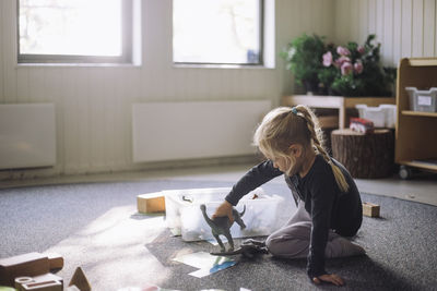 Side view of girl playing with artificial dinosaurs while sitting on carpet in classroom at kindergarten