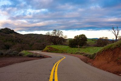 Empty road by trees against sky