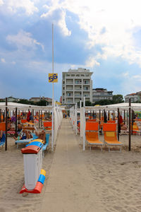 Walkway amidst deck chairs at beach against sky