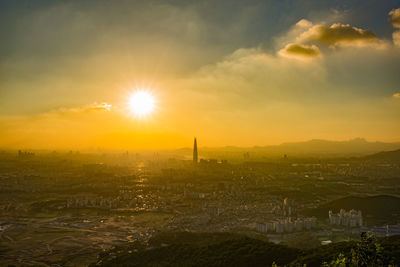 Aerial view of cityscape against bright sun in orange sky during sunrise