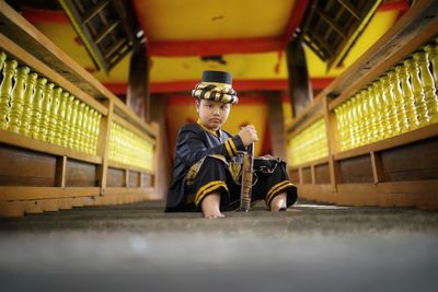 Low angle view of a boy with traditional clothes sitting on stair