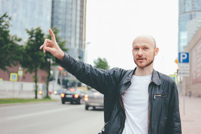 Portrait of young man hailing taxi while standing on road