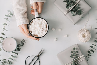 Cropped hands of woman having of hot chocolate with gifts on table