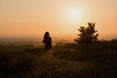 Girl standing on field against sky during sunset