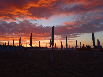 Silhouette wooden posts on beach against sky during sunset