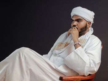 Side view of young man sitting against black background