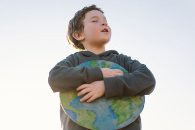 Boy embracing globe against sky