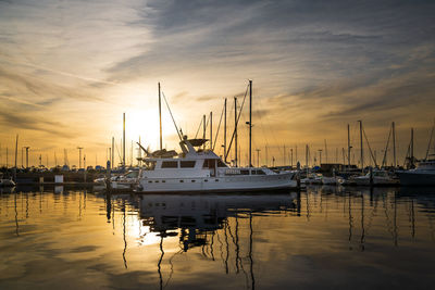 Sailboats moored at harbor against sky during sunset