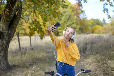 Girl taking selfie while gesturing on bicycle in forest