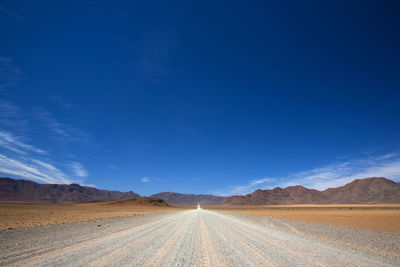 Tire tracks on desert road against blue sky