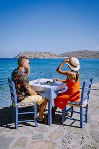 Couple sitting on chair by table against sea