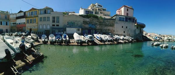 Sailboats moored on sea by buildings in city against sky