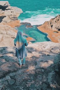 Rear view of woman standing on rock by sea