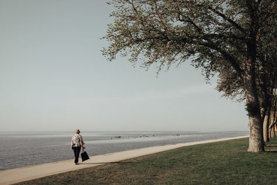 Full length rear view of senior woman walking on promenade by sea