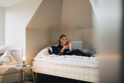 Man using mobile phone while sitting on bed at home