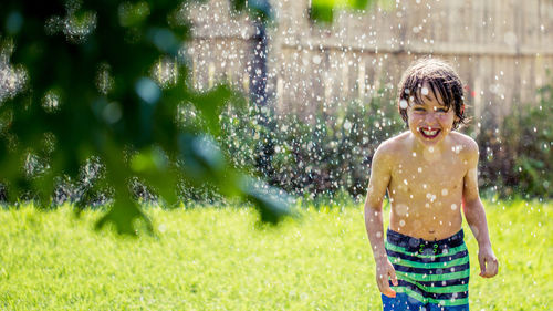 Portrait of boy enjoying in water on grassy field at yard