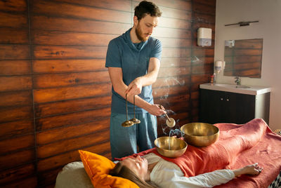 Young man holding camera while standing on bed