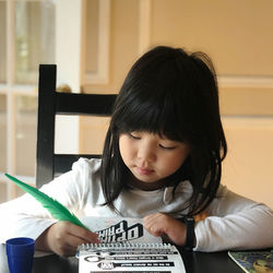 Portrait of a girl sitting on table writing