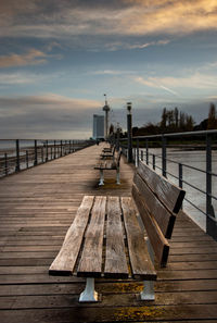 Empty bench on pier by sea against sky during sunset