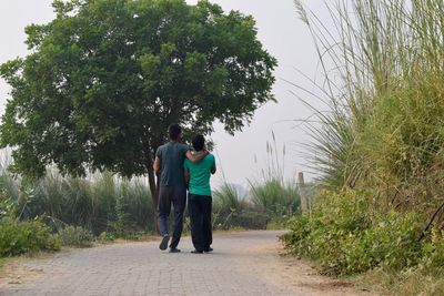 Rear view of friends walking on road against trees