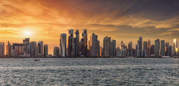 View of cityscape by sea against sky during sunset