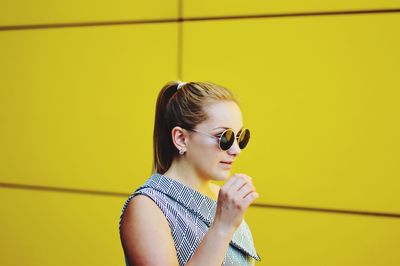 Girl wearing sunglasses standing against yellow wall