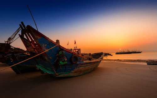 Ship moored at beach against sky during sunset