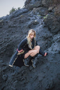 Young woman crouching on black rocky mountain