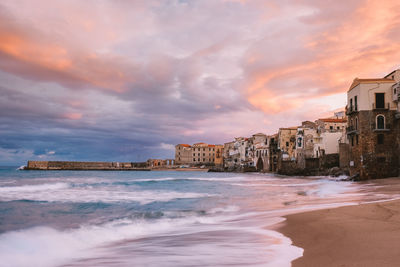 Buildings by sea against sky during sunset