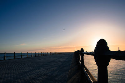 Silhouette woman on pier at beach against clear sky