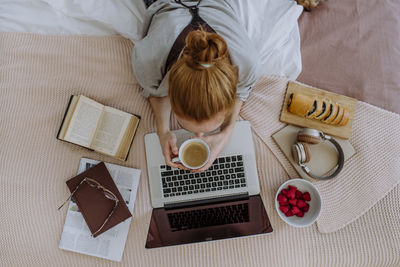Woman with coffee cup lying on bed studying through laptop at home