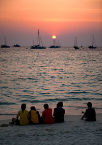 Rear view of people enjoying in sea against sky during sunset