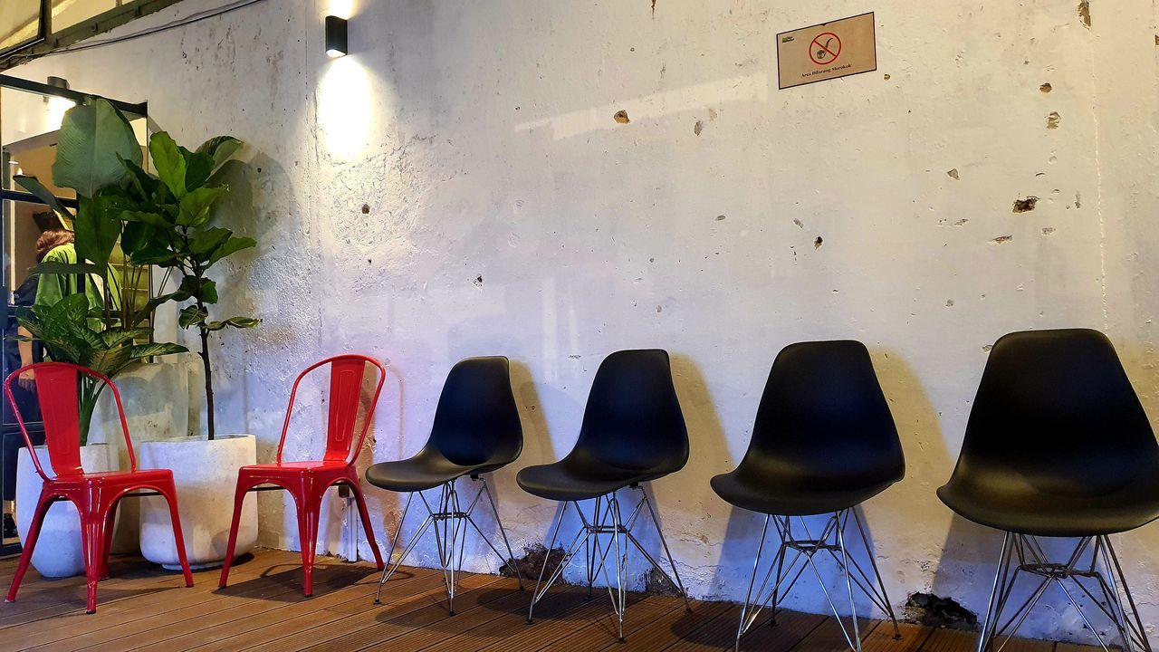 EMPTY CHAIRS AND TABLE AGAINST WHITE WALL