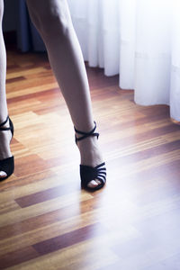 Low section of woman standing on hardwood floor at home w