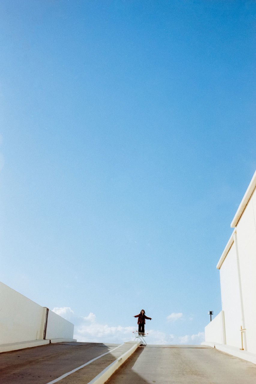 sky, copy space, one person, blue, day, architecture, nature, lifestyles, real people, rear view, clear sky, full length, men, transportation, the way forward, leisure activity, road, walking, direction, outdoors