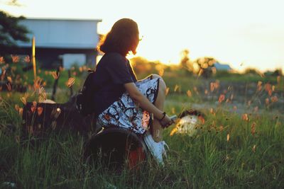 Side view of woman sitting on pipe at grassy field during sunset