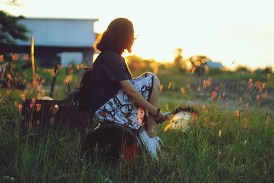 Side view of woman sitting on pipe at grassy field during sunset