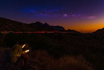 Man using mobile phone while sitting on field against star field