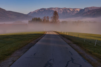 Empty road amidst field against sky