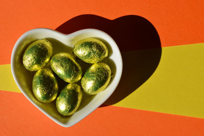 Gold foil wrapped chocolate easter eggs in heart shaped dish isolated on colorful background