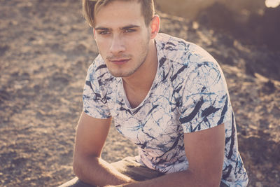 Thoughtful young man looking away while sitting on land during sunset