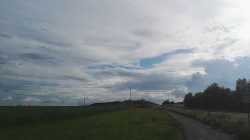 Road passing through field against cloudy sky